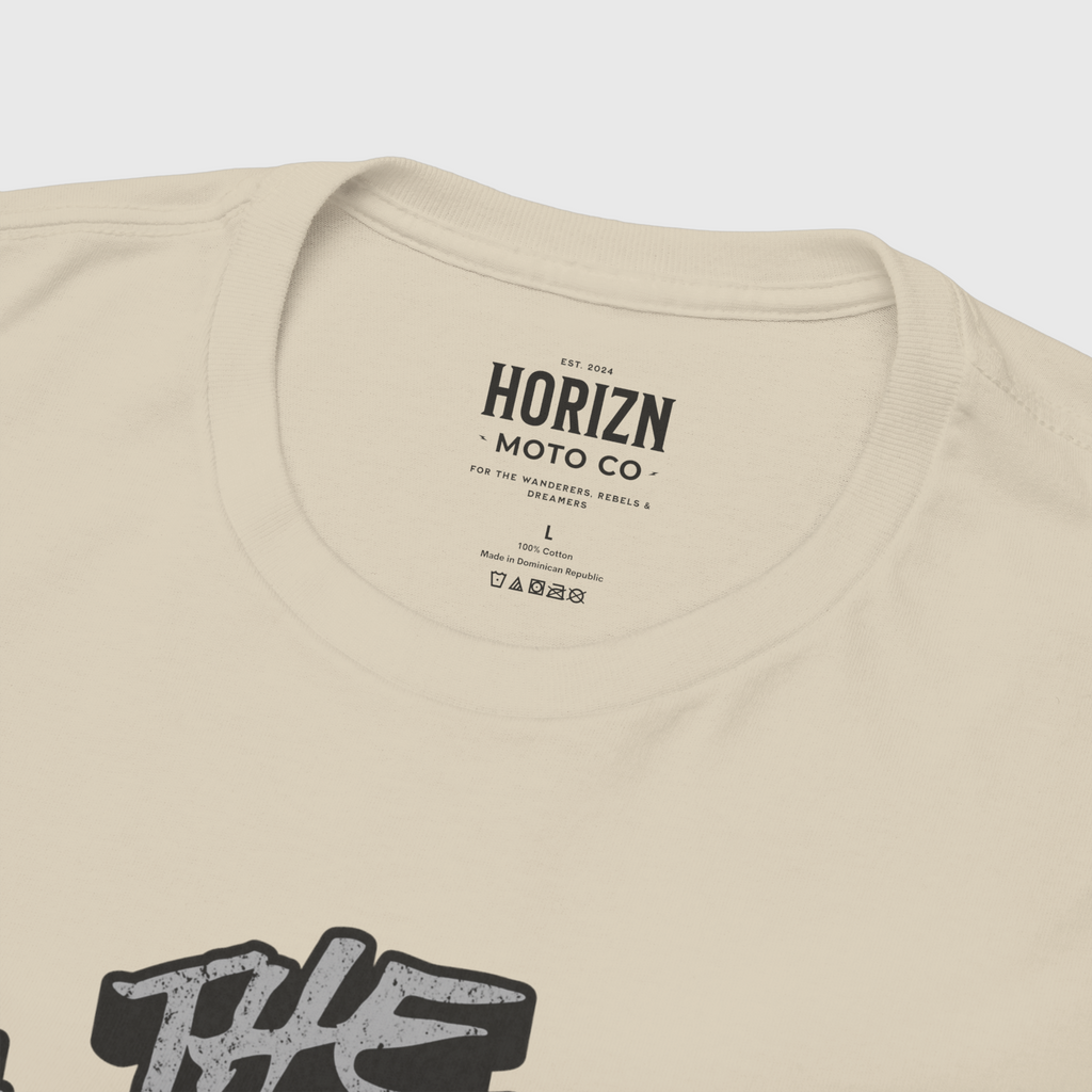 Beige graphic t-shirt featuring a skull in a helmet, worn by a man with long hair and a casual style, representing the Charge the World Skull Moto Tee. Ideal for riders and streetwear enthusiasts.