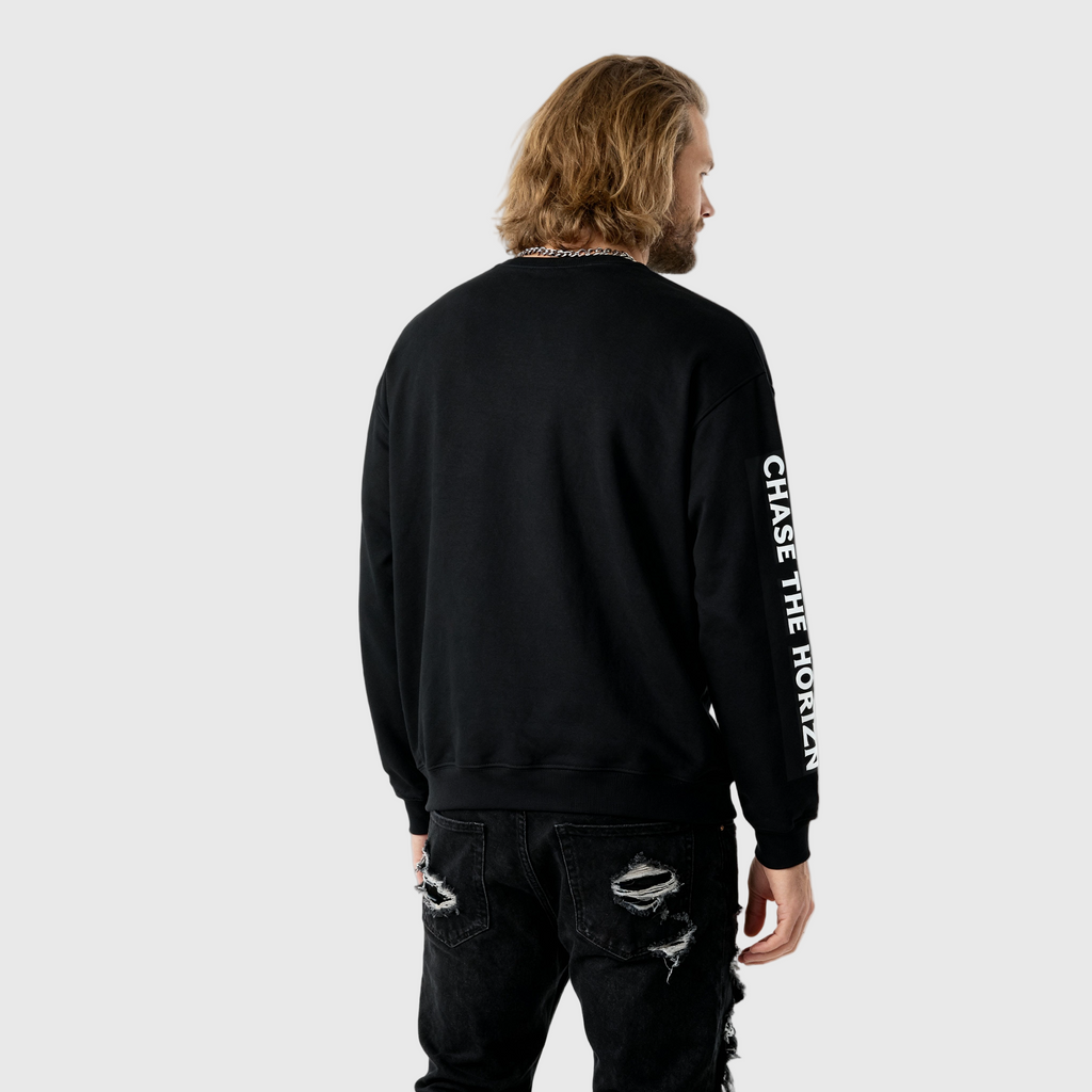 Person wearing a black long-sleeve shirt with 'CHASE THE HORIZN' text on the sleeve, standing against a white background.