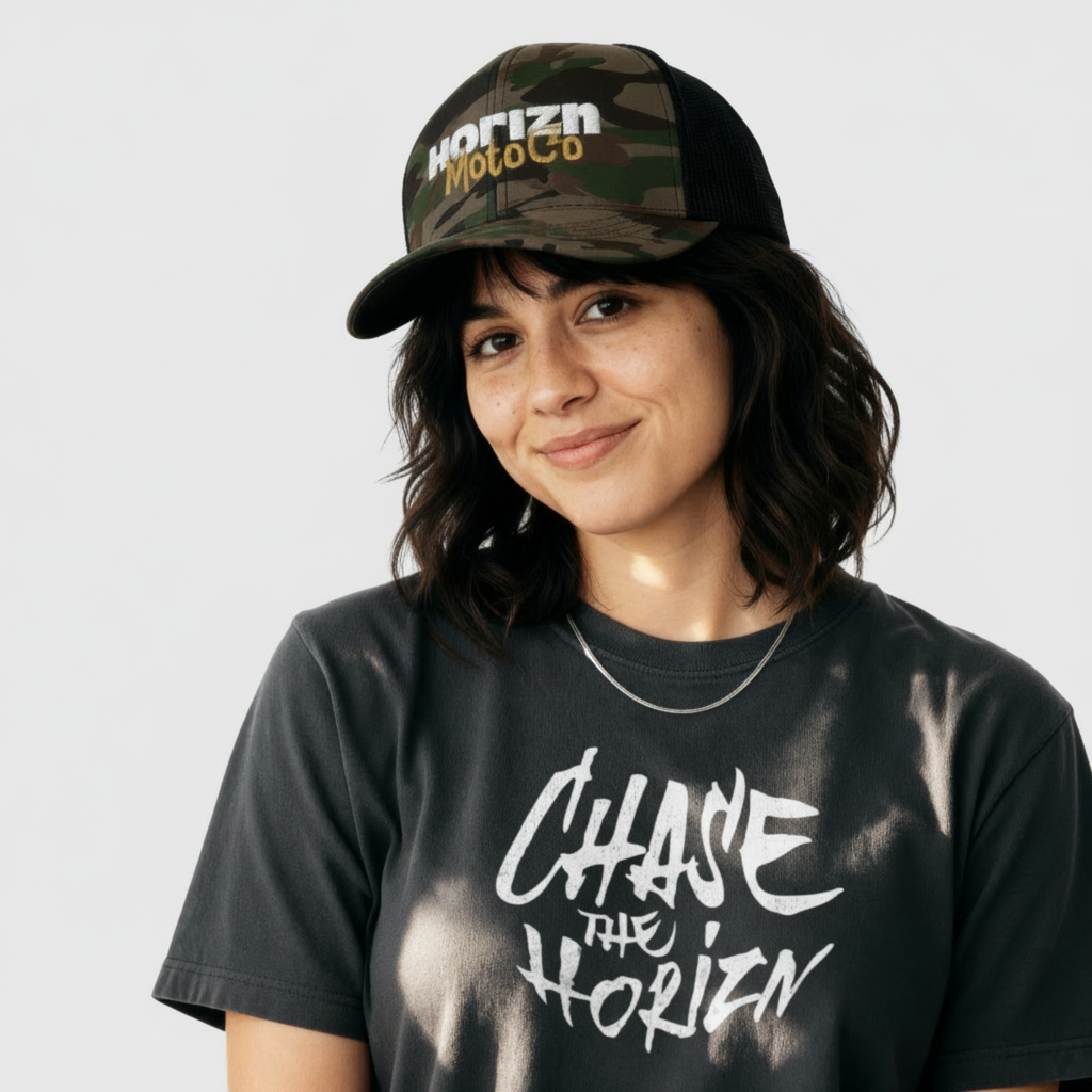 Camo Mesh Trucker Cap worn by woman with shoulder-length dark hair, featuring white 'HORIZN' logo and gold 'MotoCo' graphic, styled with gray 'CHASE THE HORIZN' t-shirt.
