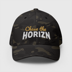 Front view of the Multicam Black camouflage Chase the HORIZN Flexfit cap, with gold-and-white embroidered lettering and a curved visor.