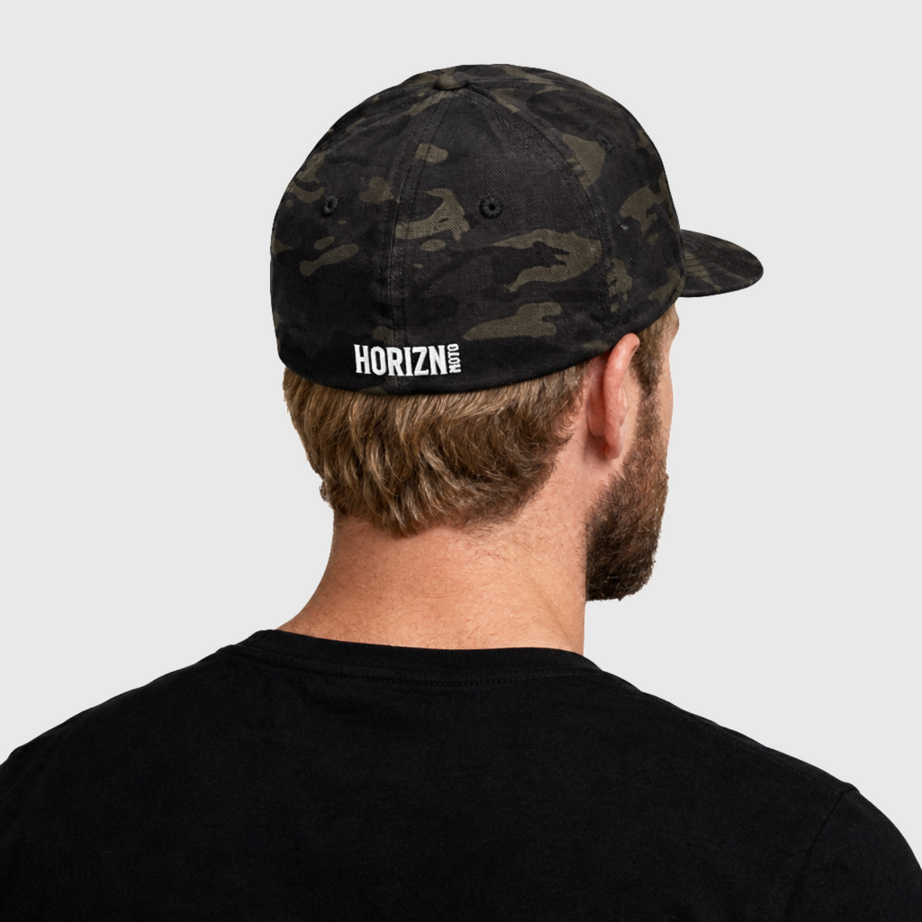 Rear three-quarter view of a model wearing the Multicam Black camouflage Chase the HORIZN Flexfit cap, showing the small white HORIZN logo embroidered on the back.